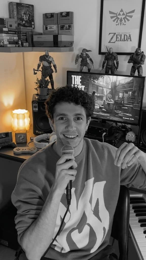 Nazareno Tondini holding a microphone in his home studio, surrounded by game collectibles