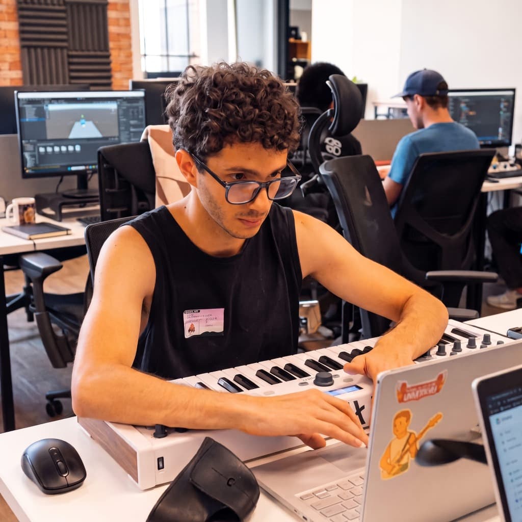 Naza playing a MIDI keyboard at his desk in a game studio